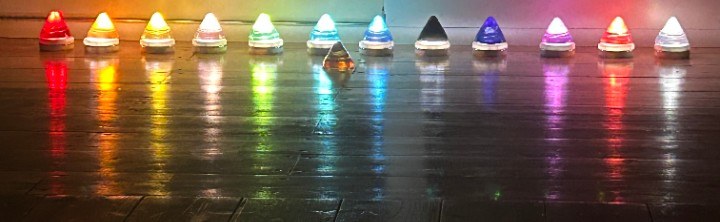 A row of small colored lights in rainbow order reflecting on a dark glossy surface